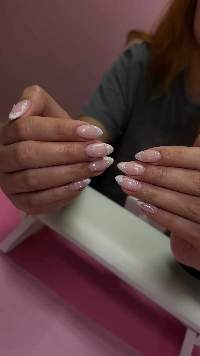 Soft pink nails with white glitter french tips and pearl accents