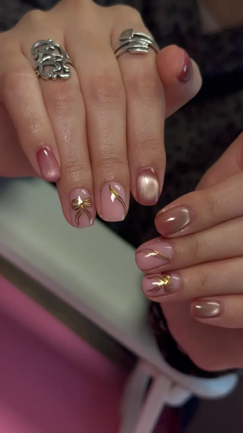 Pink chrome ombre nails with gold metallic accents and 3D gold bow
